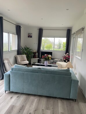 Ein modernes Wohnzimmer mit einem großen blauen Sofa, einem Flachbildfernseher, einem Couchtisch mit Blumen und einem Bücherregal.
