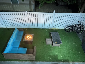 A patio with a blue sofa, a small table with a fire feature, and a wicker table.