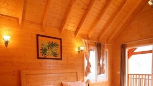 A wooden cabin room with a bed, nightstands, and a window with curtains. - The Auli Meadows (Joshimath)