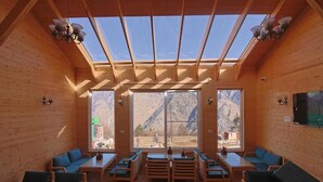 A wooden interior with a skylight, large windows, and seating areas. - The Auli Meadows (Joshimath)