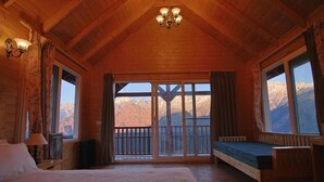 A wooden cabin room with a bed, a bench, and a balcony with mountain views. - The Auli Meadows (Joshimath)