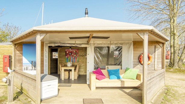 A wooden beach house with a covered patio, a dining area, and a sofa with colorful cushions. - Beachside Dune Home Retreat for 4 (Almere)