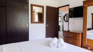 Ein Hotelzimmer mit einem Bett, zwei Holztüren, einem Schminktisch und einem Fernseher.