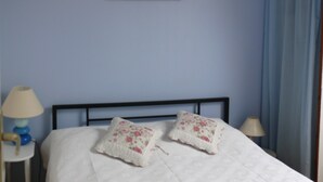 Ein Bett mit zwei blumigen Kissen, ein Nachttisch mit Lampe und eine Wand mit einem Blumenbild.