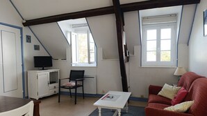 Ein Zimmer mit schrägen Wänden, einem weißen Schreibtisch, einem roten Sofa, einem gemusterten Teppich und einem Fenster mit Blick.