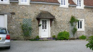 Ein Steinhaus mit weißer Tür, einem kleinen Fenster und einer Schotterauffahrt.