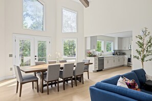 Eine moderne Küche mit weißen Schränken, ein Essbereich mit einem Holztisch und Stühlen sowie ein blaues Sofa.