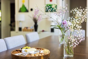 Ein Esstisch mit einer Holzplatte, die Käse, Cracker und Nüsse trägt, sowie einer Vase mit Blumen.