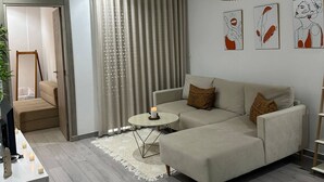 A modern living room with a sectional sofa, a small round table, and a hanging pendant light. - Cozy Hammamet Apartment Beach, Pool, and Comfort Await (Hammamet)
