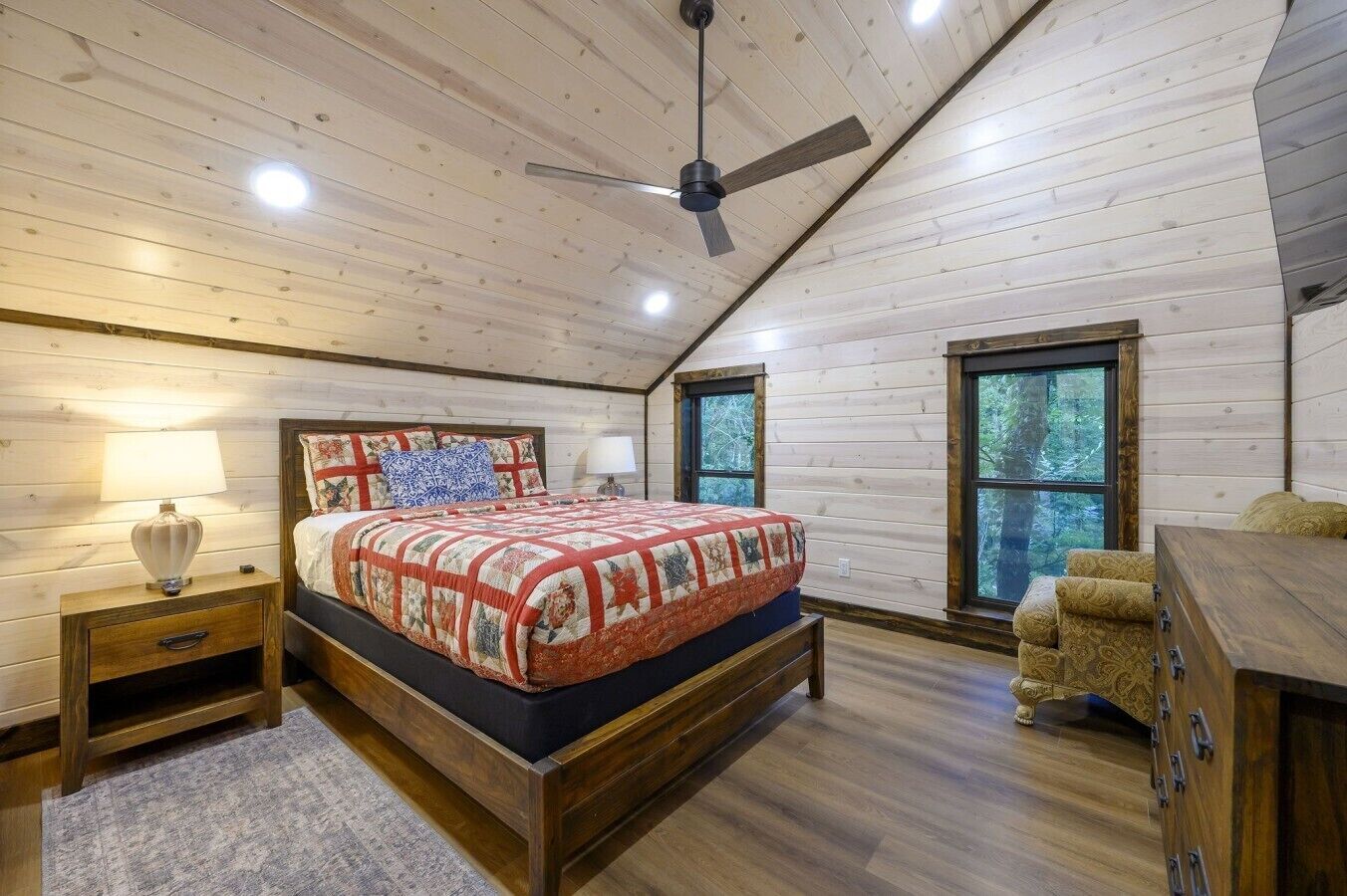Un dormitorio con techo de madera, cama con colcha, mesita de noche, cómoda y ventana.
