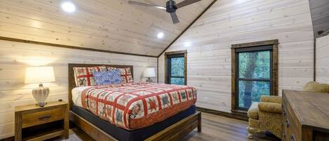 Un dormitorio con techo de madera, cama con colcha, mesita de noche, cómoda y ventana.