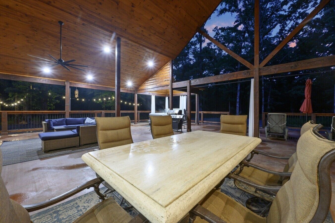 Een overdekt terras buiten met een eettafel, stoelen en een plafondventilator.