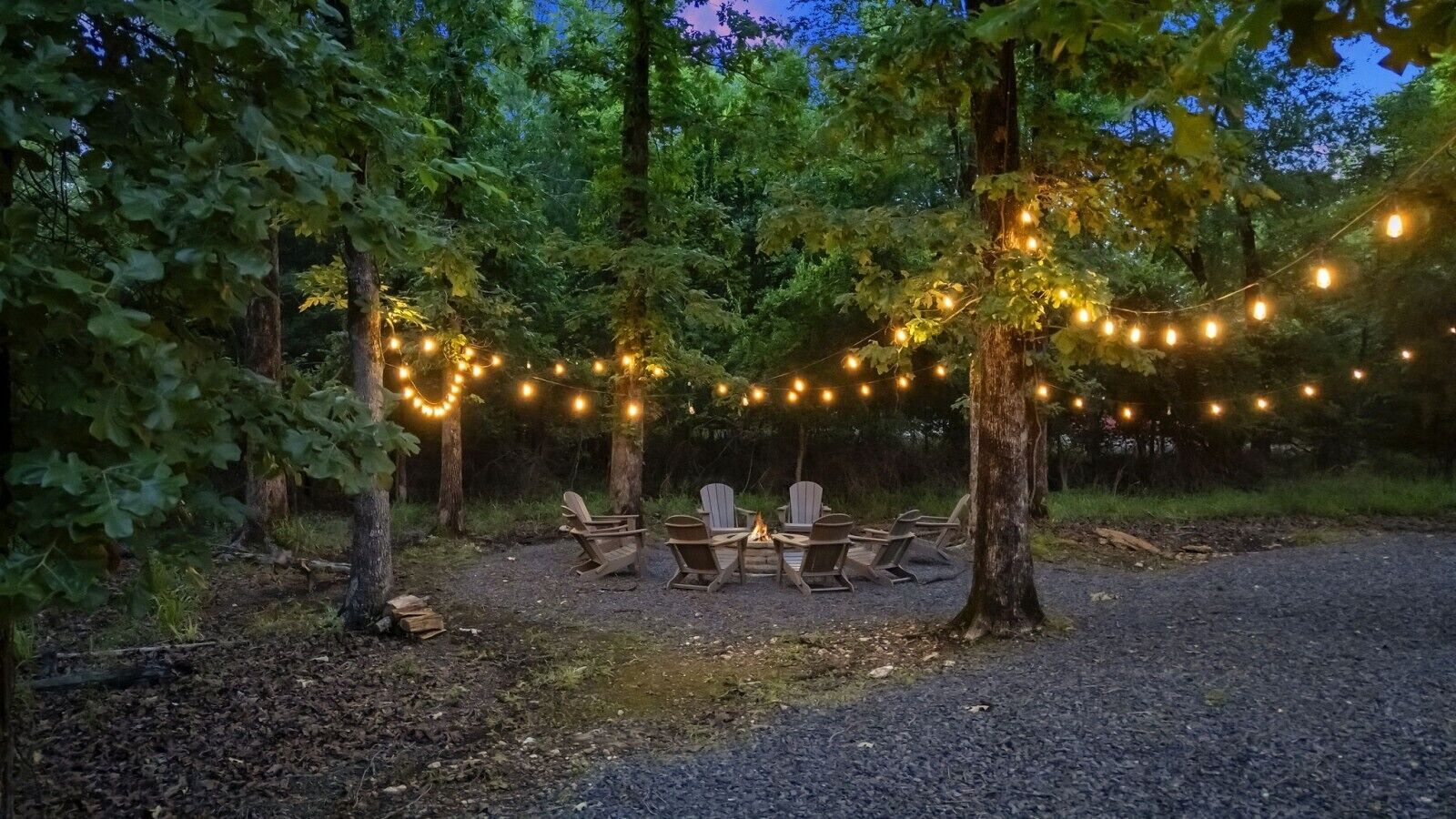 Un área boscosa con luces colgantes, asientos al aire libre y una chimenea.