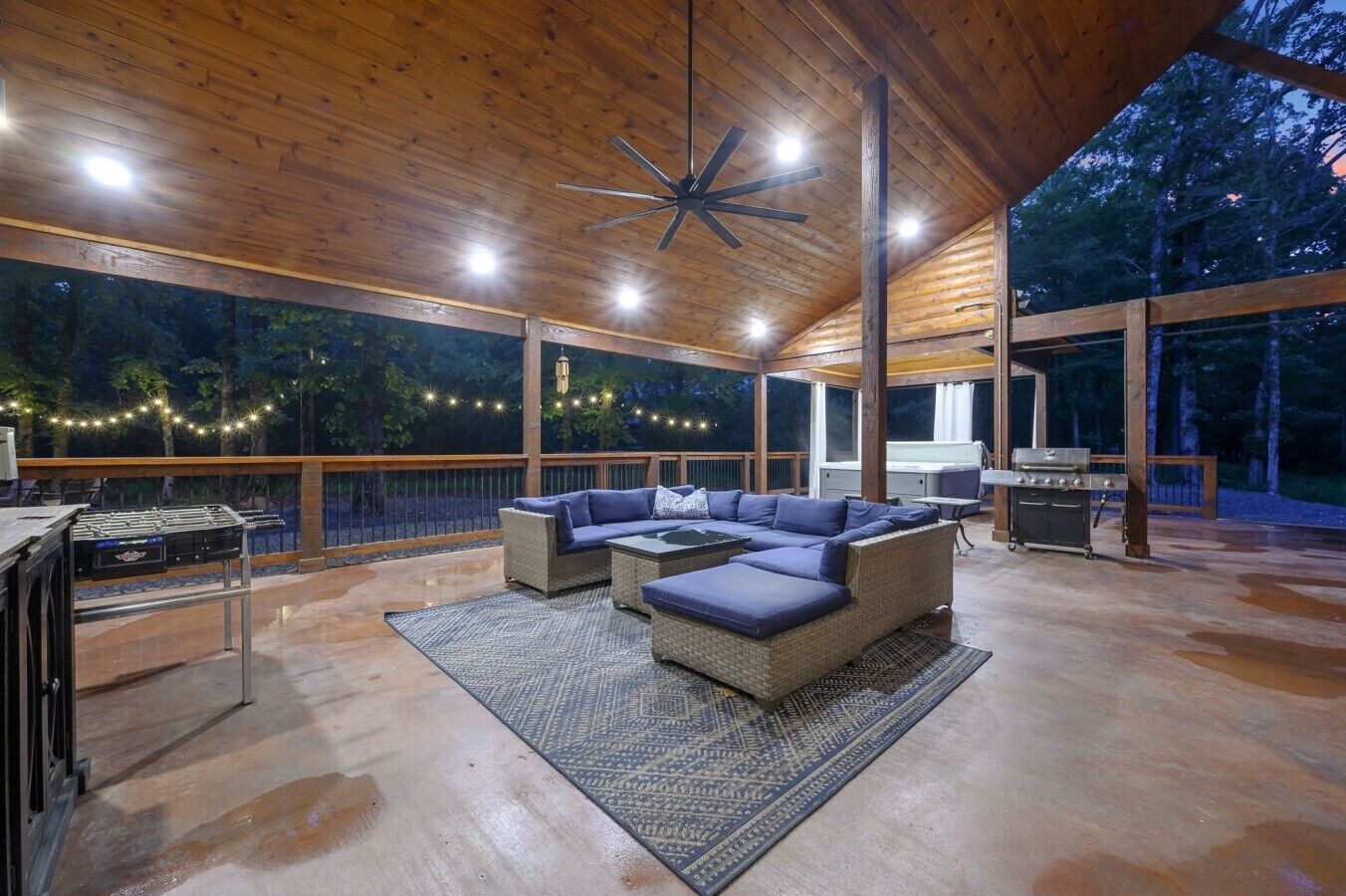 Une terrasse extérieure avec un canapé d’angle, un barbecue et des guirlandes lumineuses.