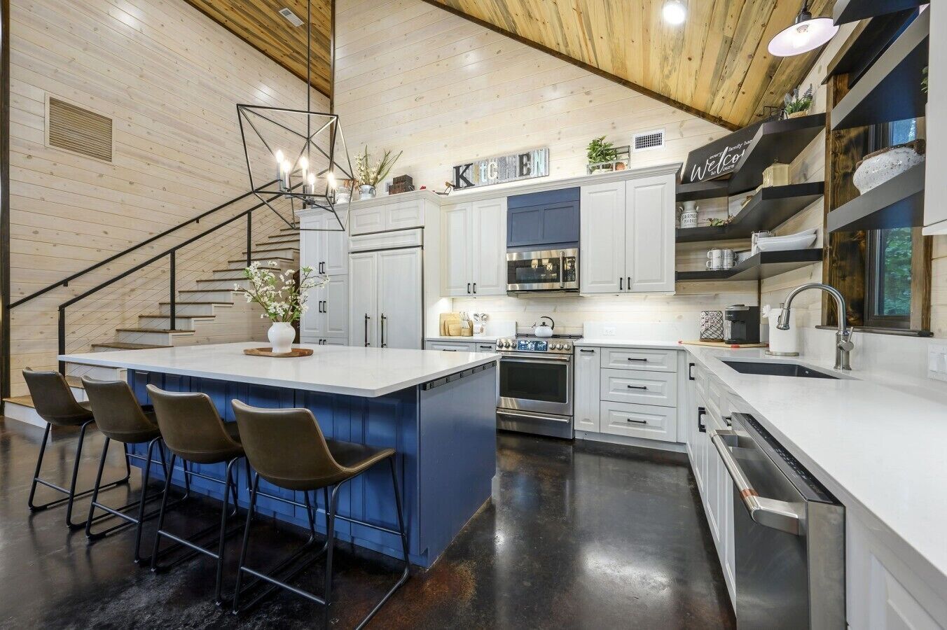 Una cocina moderna con una isla central, taburetes de bar, horno empotrado y microondas.