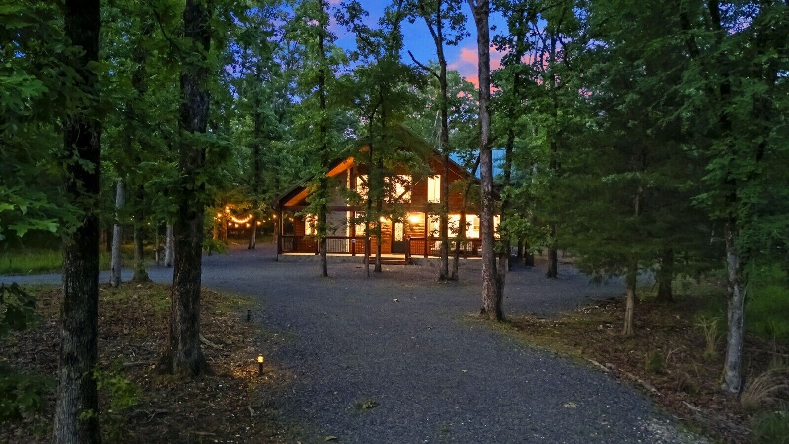 Un chalet avec une allée en gravier, entouré d’arbres, et une terrasse en bois à l’avant.