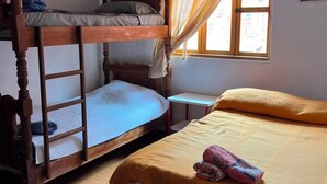 A room with a bunk bed, a single bed, a small table, and a window with curtains.