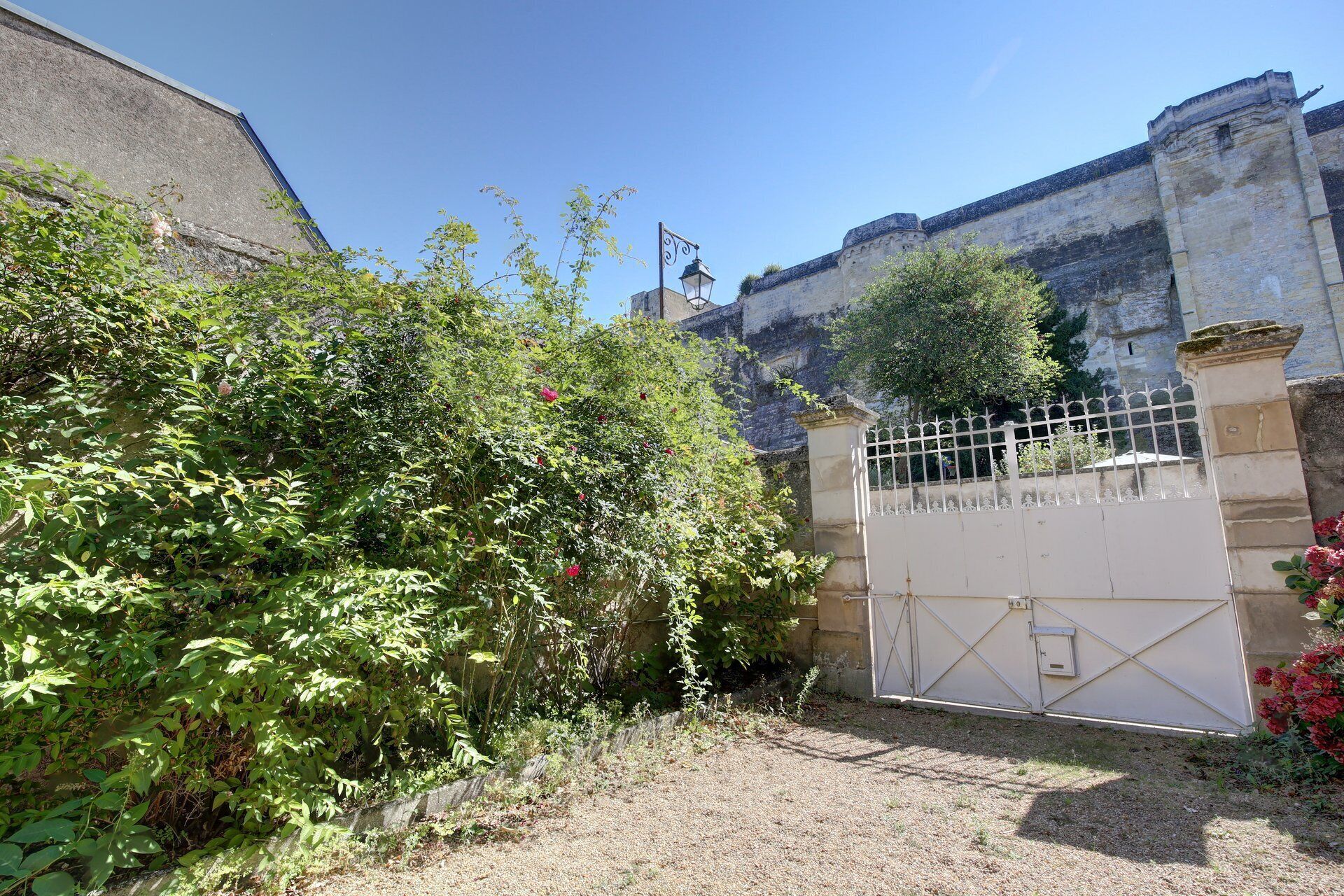 Ein verschlossenes Tor mit einer Steinmauer, einem Metallgitter und einem kleinen Baum.