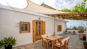 Eine Terrasse mit Steinboden, Holzmöbeln und einer Pergola.
