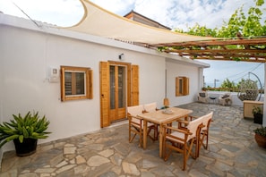 Un patio con suelo de piedra, muebles de madera y una pérgola.