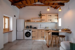 Una cocina compacta con muebles de madera, lavadora y un taburete.