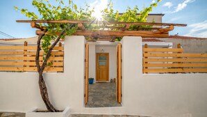 Ein weißes Gebäude mit einer Holz-Pergola, einem gepflasterten Eingangsbereich und einem Holzzaun.