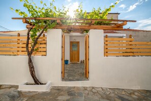 Un edificio blanco con una pérgola de madera, un acceso empedrado de piedra y una valla de madera.