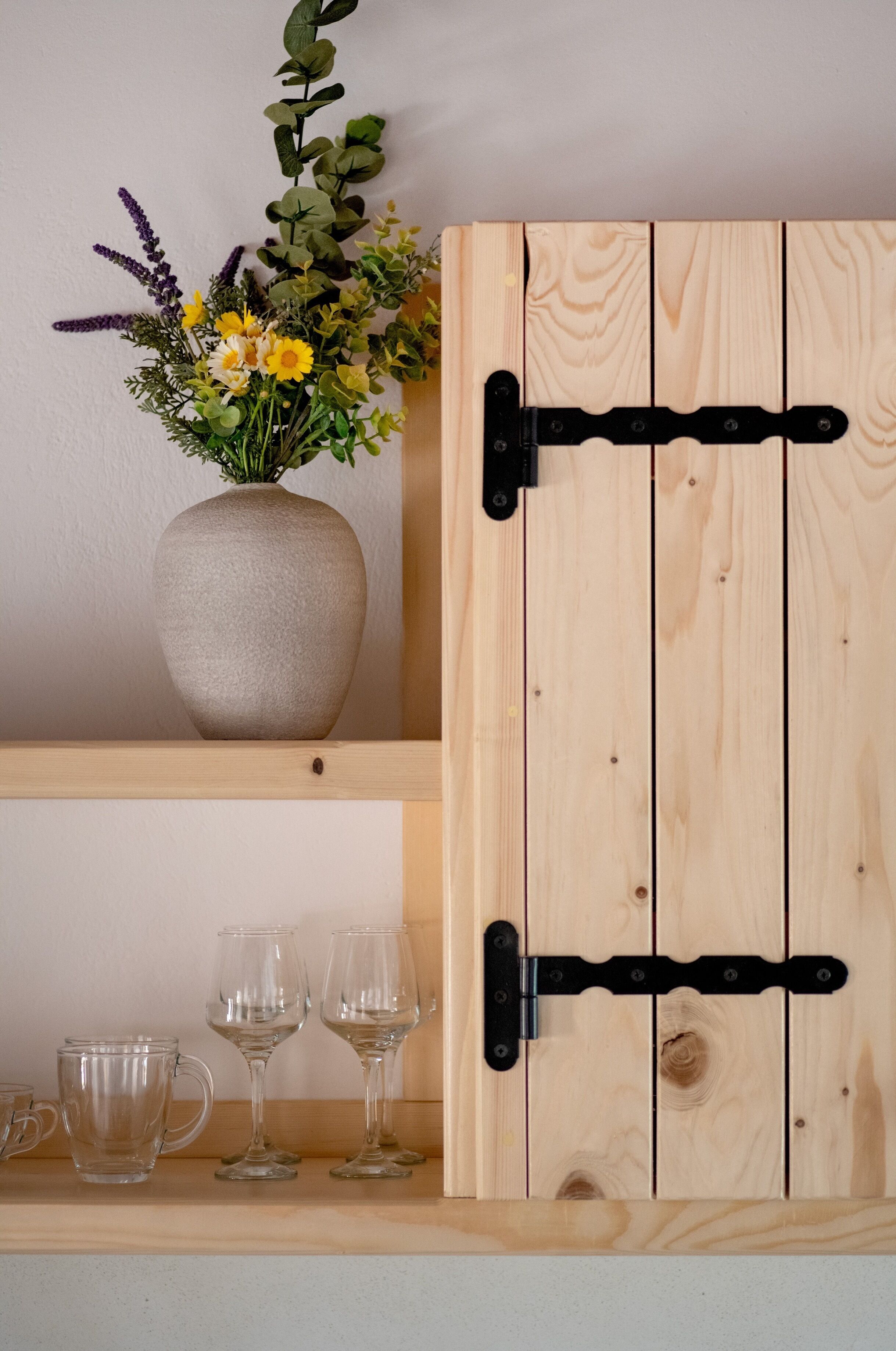 Un mobiletto in legno con un vaso di fiori e tre bicchieri di vetro su uno scaffale.
