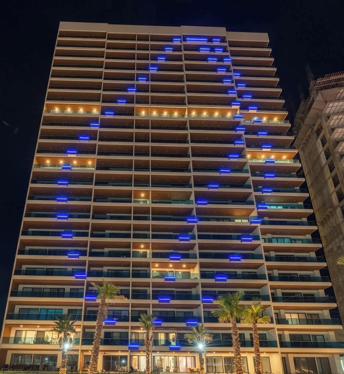 A multi-story hotel with a modern design, featuring balconies and a distinctive lighting pattern on the facade.