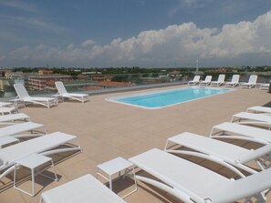 Una piscina sul tetto con poltrone da relax bianche e una vista aperta sui palazzi circostanti.