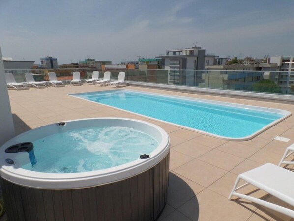 Area piscina sul tetto con vasca idromassaggio e lettini.