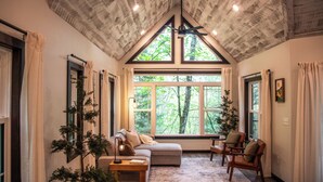A cozy room with a sloped ceiling, large windows, a sofa, chairs, and a small table.