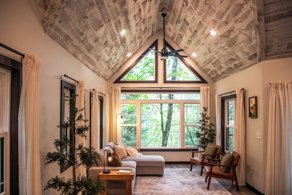 A cozy room with a sloped ceiling, large windows, a sofa, chairs, and a small table.