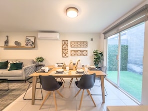 A dining area with a table set for two, a sofa, and a large window with a view of a garden. - Lujosa casa de 3 cuartos (Jardines de la Silla)
