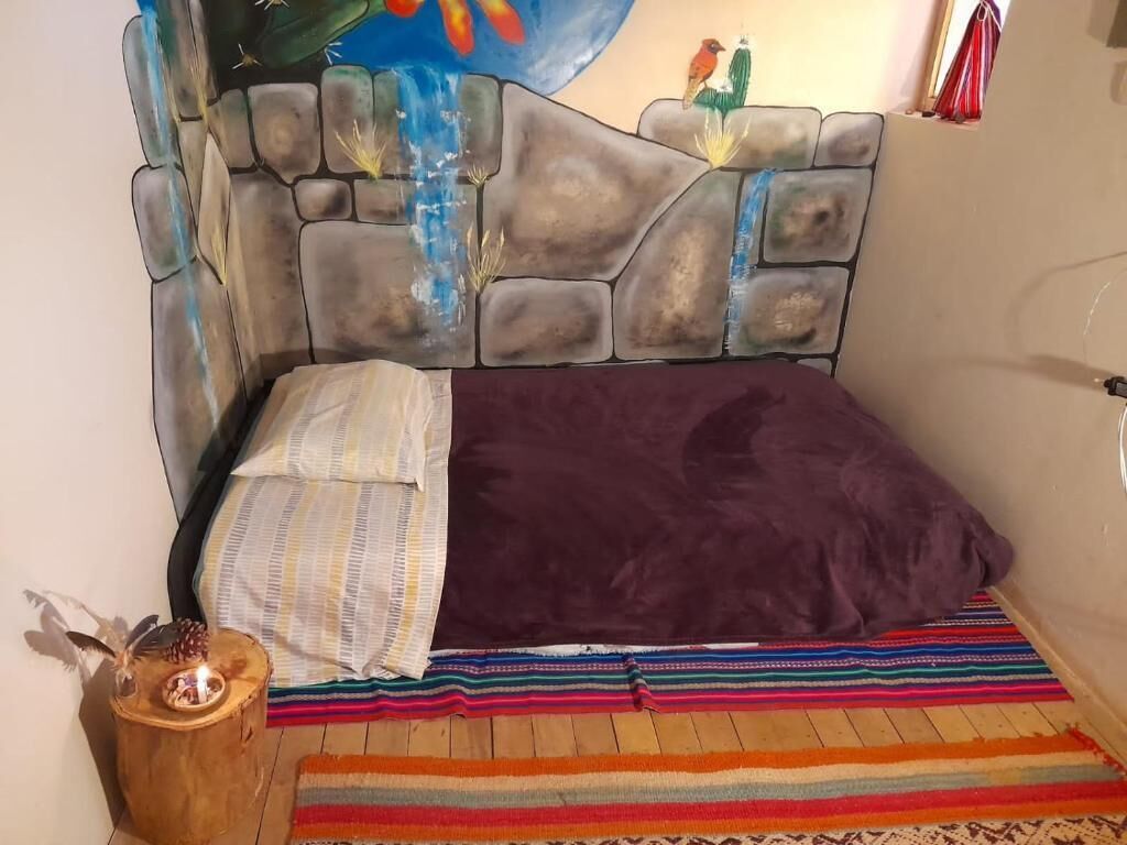 A bed with a stone headboard, a colorful striped rug, and a small wooden nightstand with a candle.