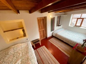 Ein Schlafzimmer mit zwei Betten, einer Holztür, einem kleinen Tisch und einem Fenster.