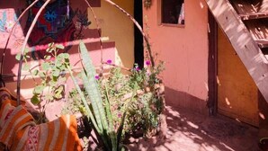 Un patio con una escalera de madera, un ventanal pequeño y un mural colorido en la pared.