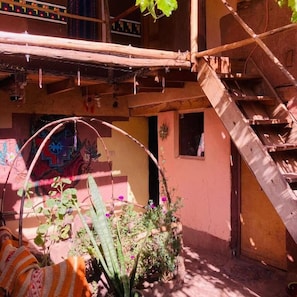Un patio con una escalera de madera, un ventanal pequeño y un mural colorido en la pared.