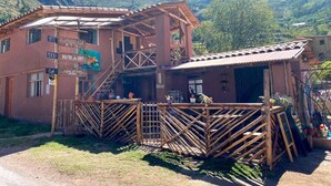 Un edificio rústico con escalera de madera, un espacio de estar al aire libre cubierto y montañas al fondo.