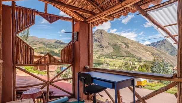 Una habitación rústica de madera con un escritorio y una silla, vistas a montañas y un techo de chapa corrugada.