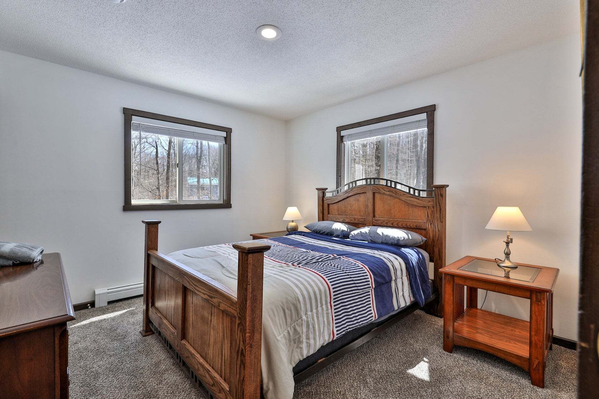 Une chambre à coucher avec un lit en bois, deux tables de chevet, une fenêtre et un sol recouvert d’une moquette.
