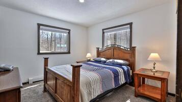 Une chambre à coucher avec un lit en bois, deux tables de chevet, une fenêtre et un sol recouvert d’une moquette.
