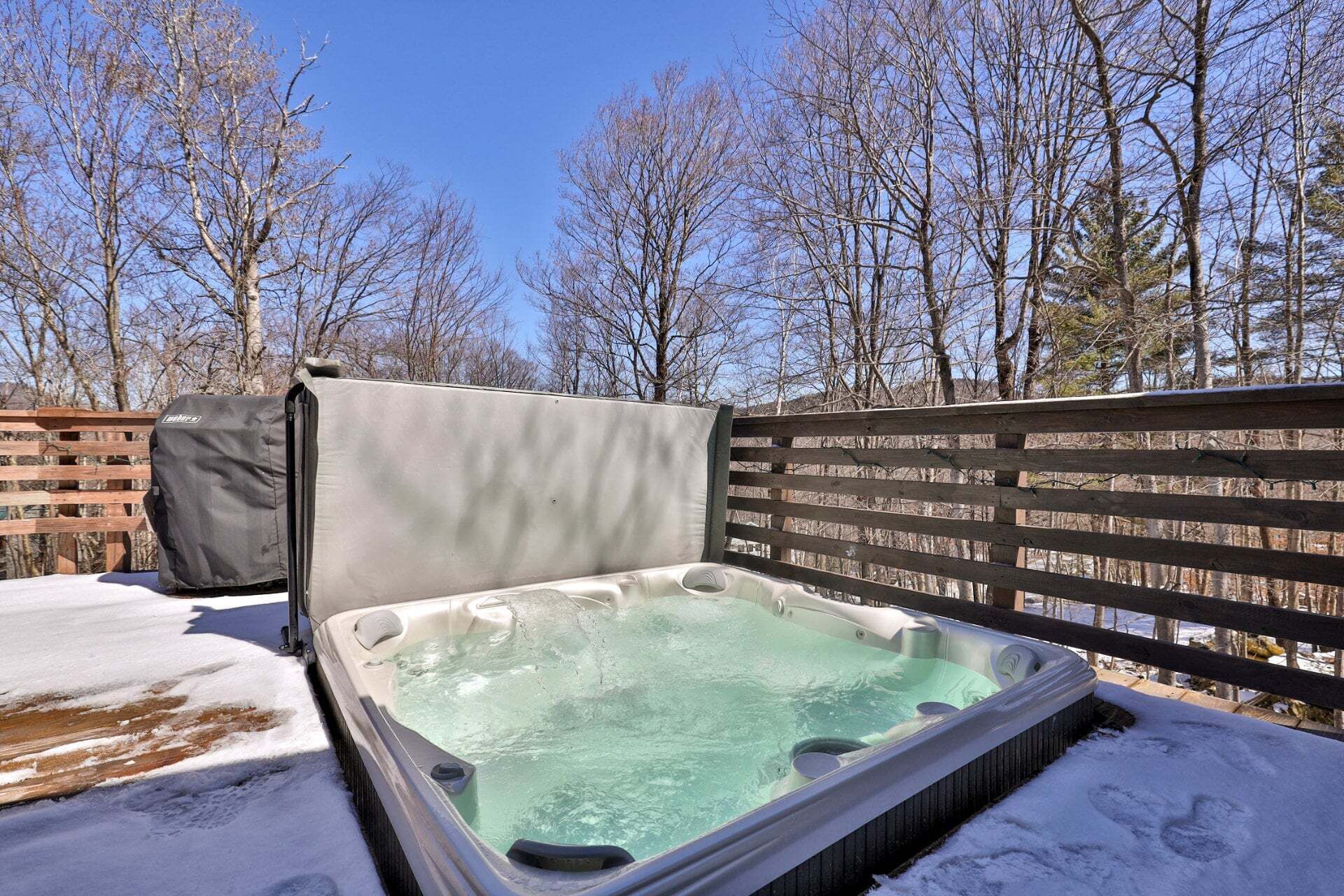 Un bain à remous en plein air, entouré d’une clôture en bois et avec des arbres sans feuilles en arrière-plan.