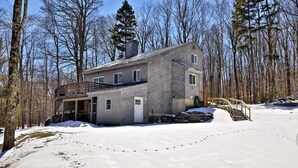 A two-story house with a deck, surrounded by a snowy landscape and trees. - Liquid Lodge Lower: 2BR Duplex near Killington with 4 PM Checkout (Killington)