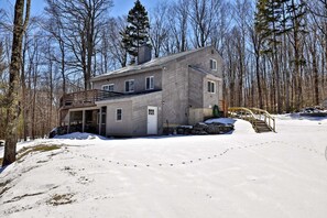 Ein zweistöckiges Haus mit einer Terrasse, umgeben von verschneiter Landschaft und Bäumen.