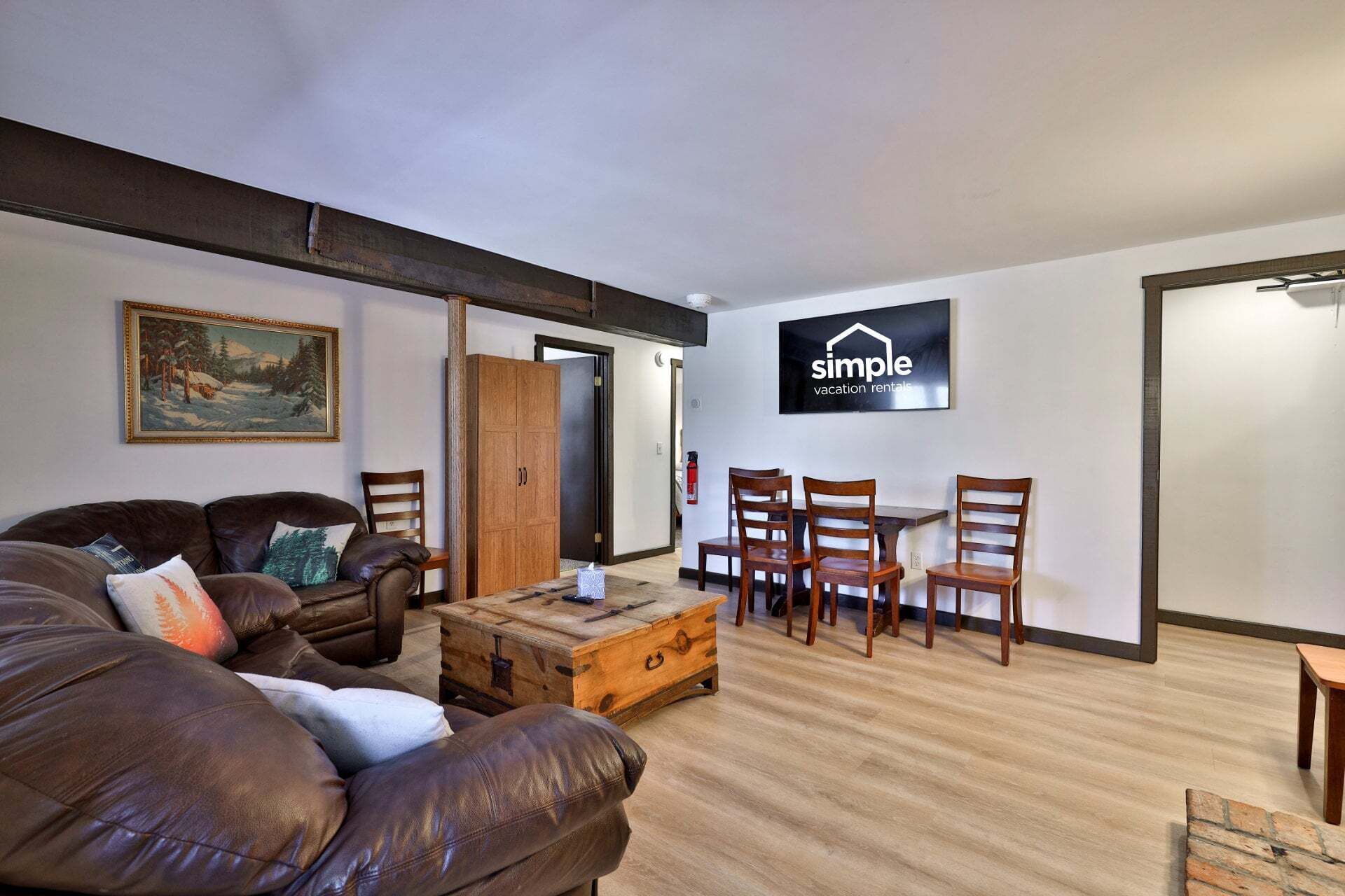 A furnished living room with a sofa, a wooden coffee table, and a dining table with chairs. A painting is on the wall, and a sign for 'simple vacation rentals' is visible.