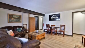 A furnished living room with a sofa, a wooden coffee table, and a dining table with chairs. A painting is on the wall, and a sign for 'simple vacation rentals' is visible. - Liquid Lodge Lower: 2BR Duplex near Killington with 4 PM Checkout (Killington)