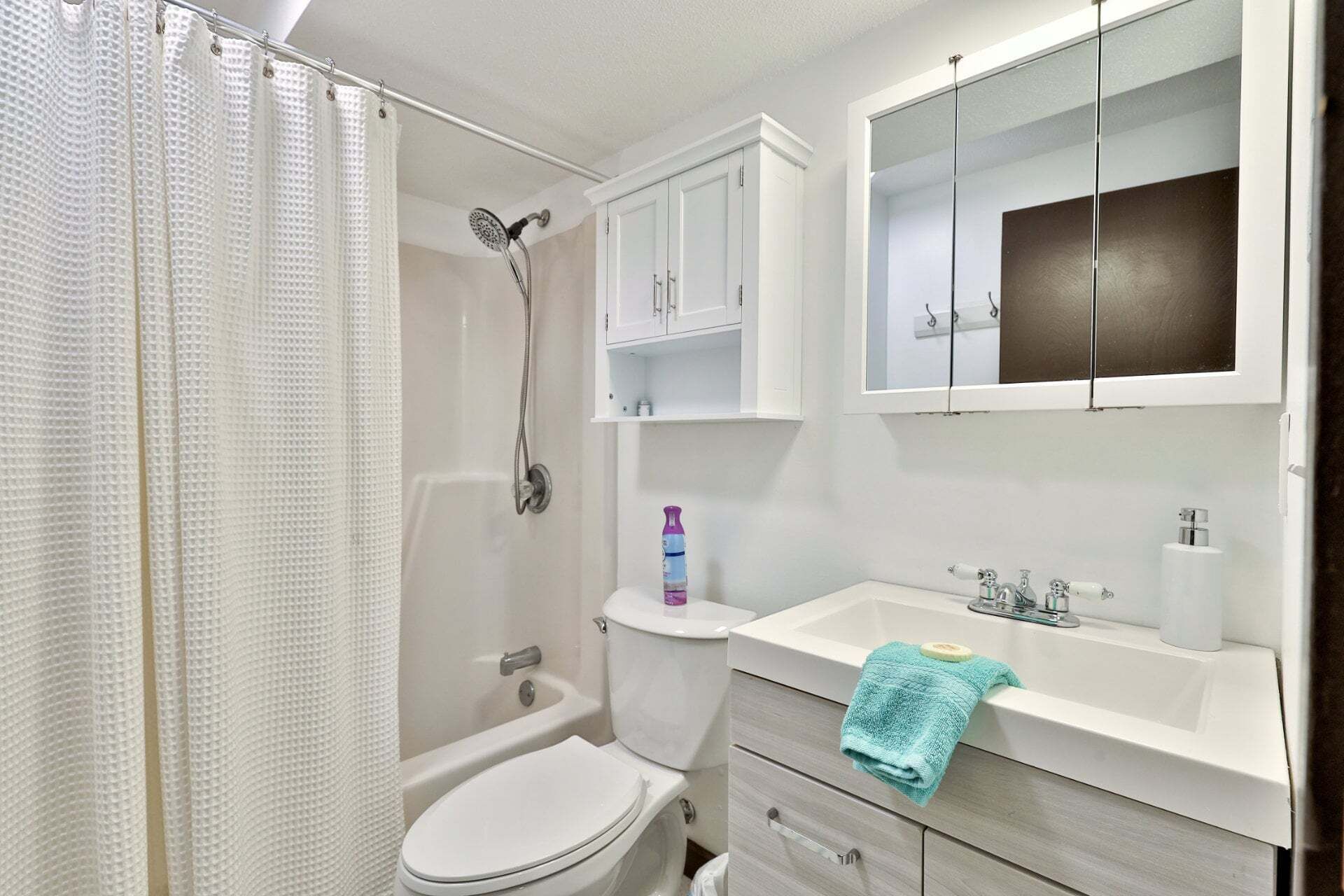 A bathroom with a shower, toilet, sink, and cabinets.