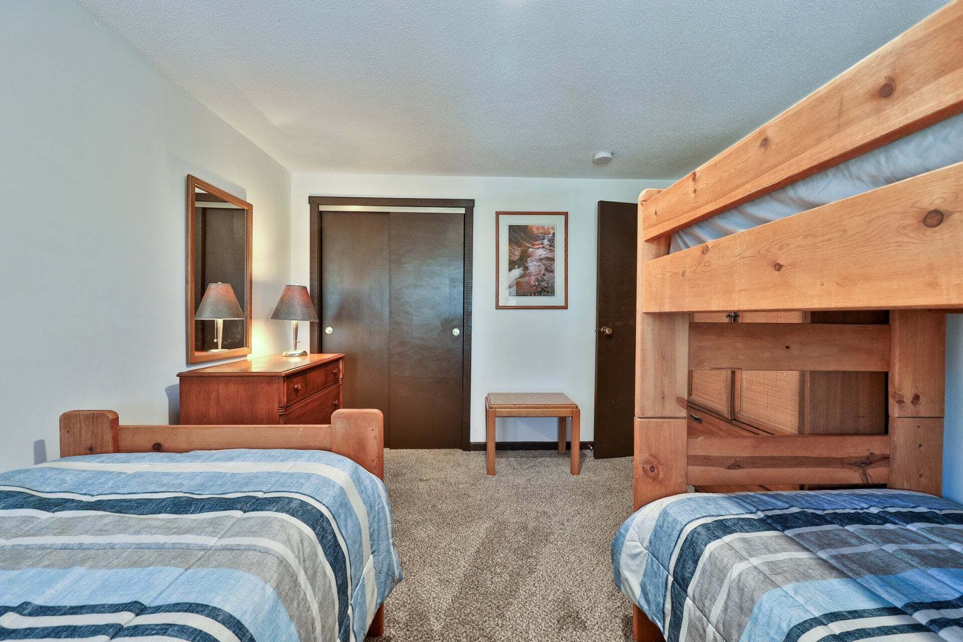 A bedroom with two beds, a dresser, a mirror, a door, and a small table.