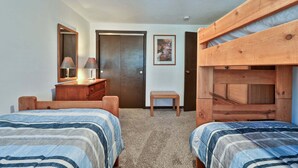 A bedroom with two beds, a dresser, a mirror, a door, and a small table. - Liquid Lodge Lower: 2BR Duplex near Killington with 4 PM Checkout (Killington)